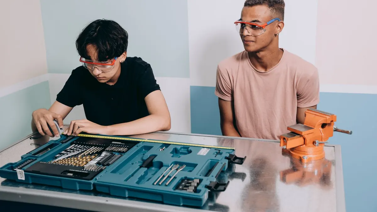 Two workshop trainees wearing safety glasses at a metal fabrication bench